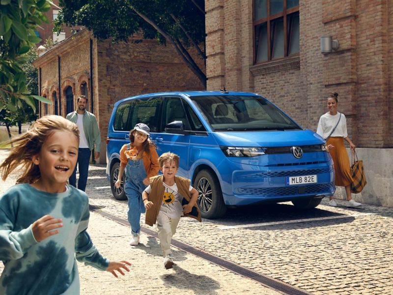 Glada barn framför en blå VW Multivan eHybrid minibuss