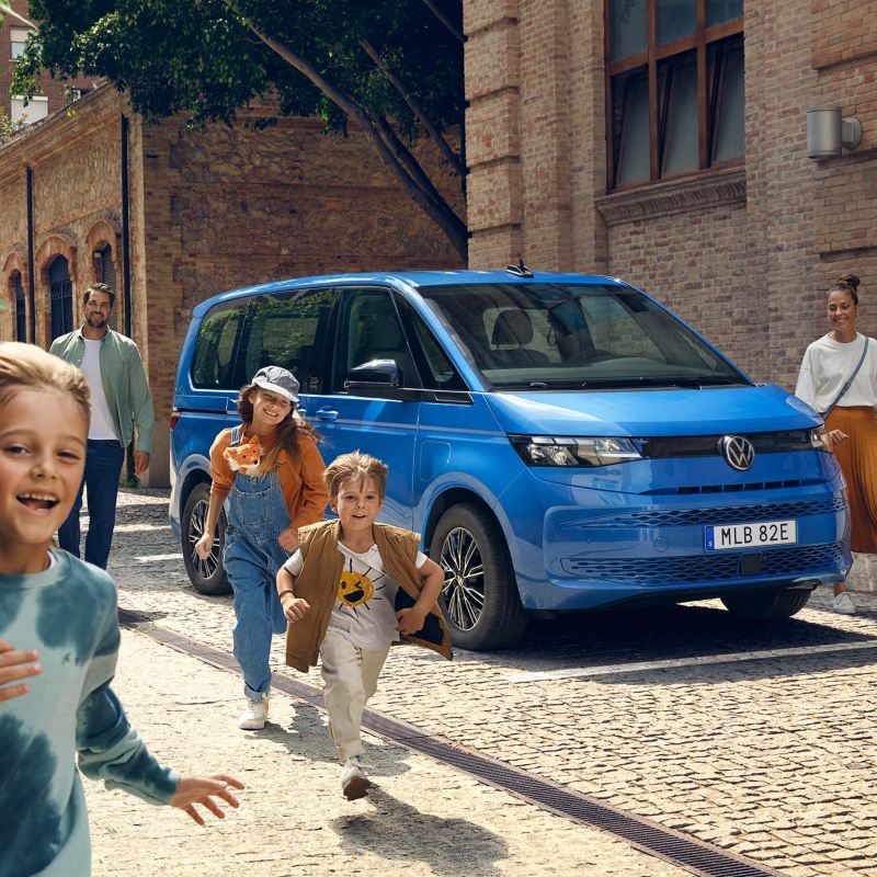 Glada barn framför en blå VW Multivan eHybrid minibuss
