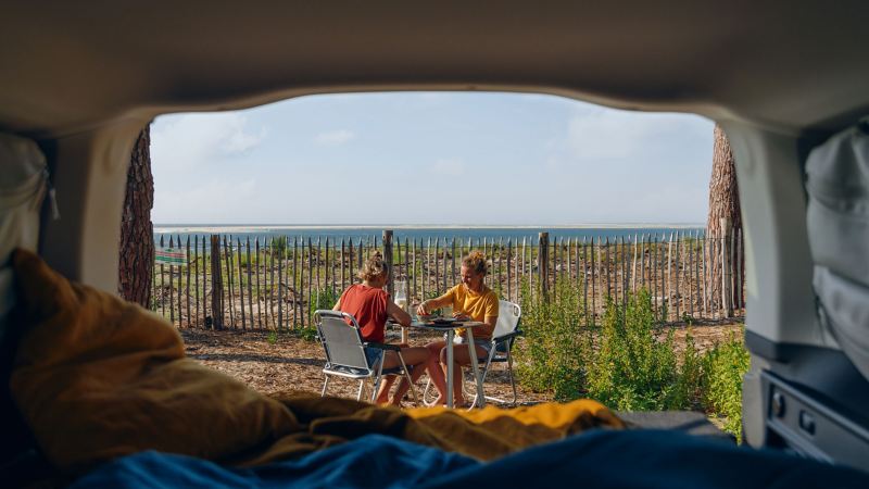 Två kvinnor äter mat vid en VW Caddy California campingbil