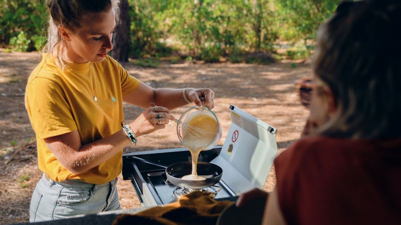 Två kvinnor lagar mat i det utdragbara pentryt en VW Caddy California campingbil