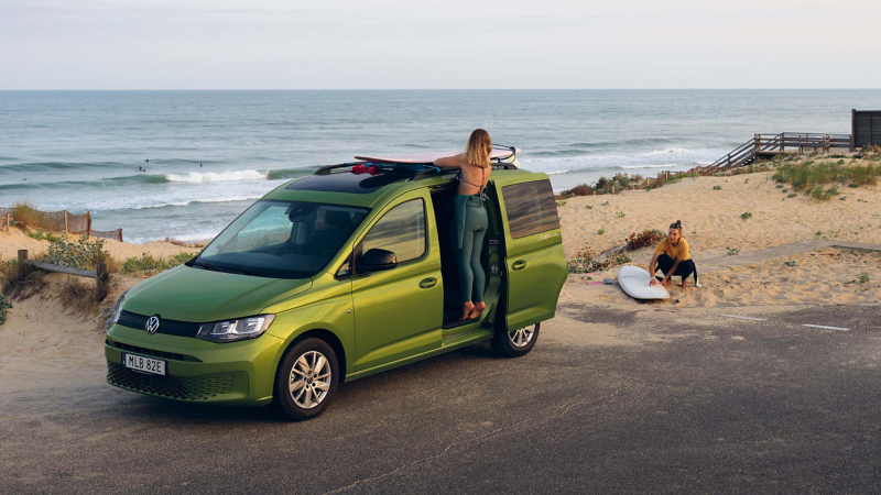 En grön VW Caddy California minihusbil parkerad vid en strand med skjutdörren öppen