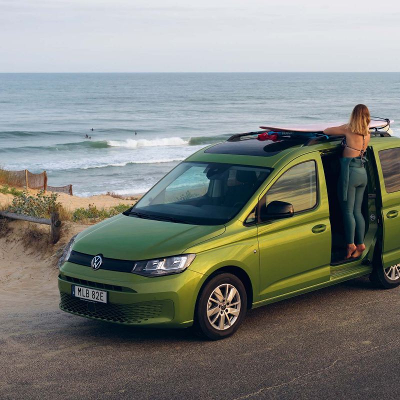 En grön VW Caddy California minihusbil parkerad vid en strand med skjutdörren öppen