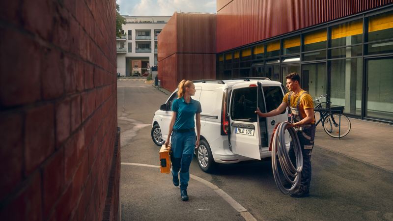 En man öppnar bakdörren på en VW Caddy Cargo skåpbil och pratar med en kvinnlig hantverkare
