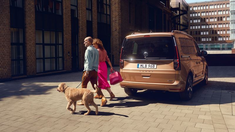 En man och kvinna går med sin hund vid en VW Caddy familjebil