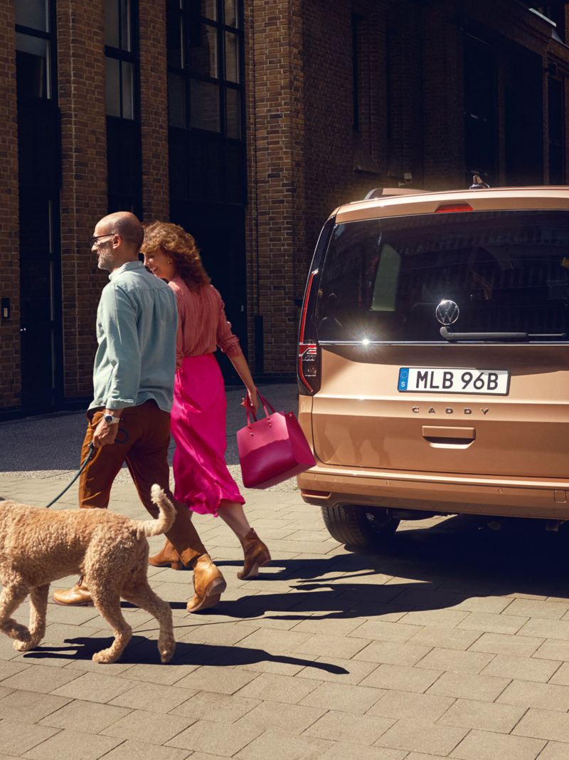 En man och kvinna går med sin hund vid en VW Caddy familjebil