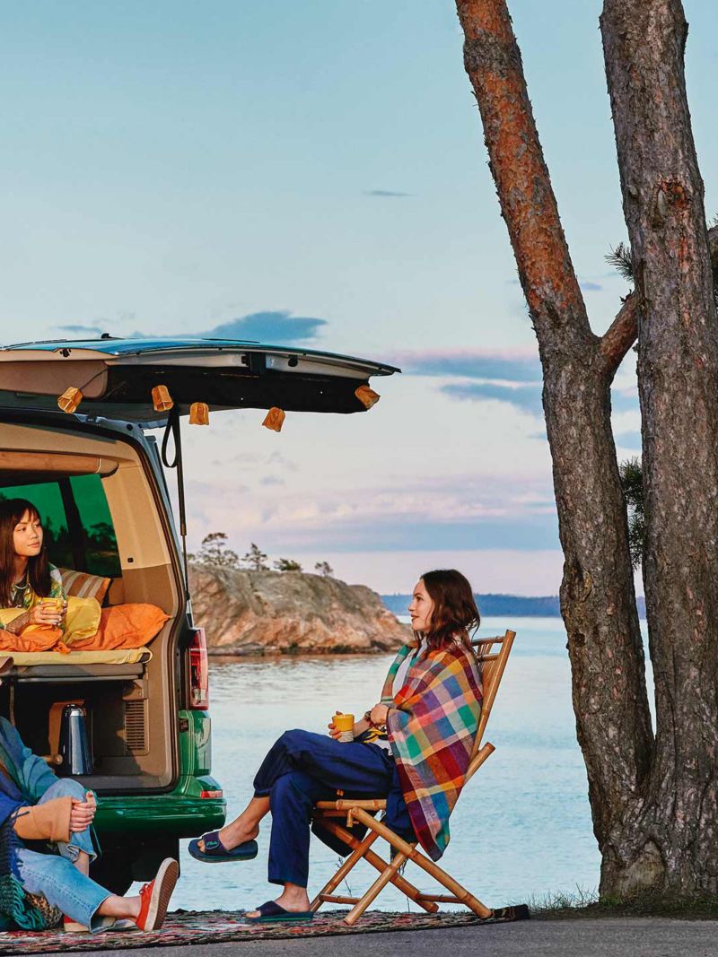 Kvinnor campar utanför en VW California 6.1 campingbil