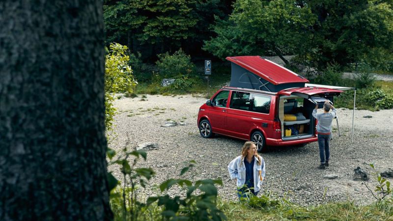 Ett par utanför en VW California campingbil, ställer upp bilen på en grusparkering