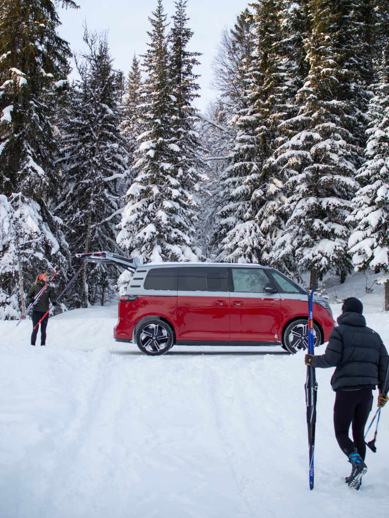 Man och kvinna med skidor står vid en VW ID. Buzz GTX i vinterlandskap