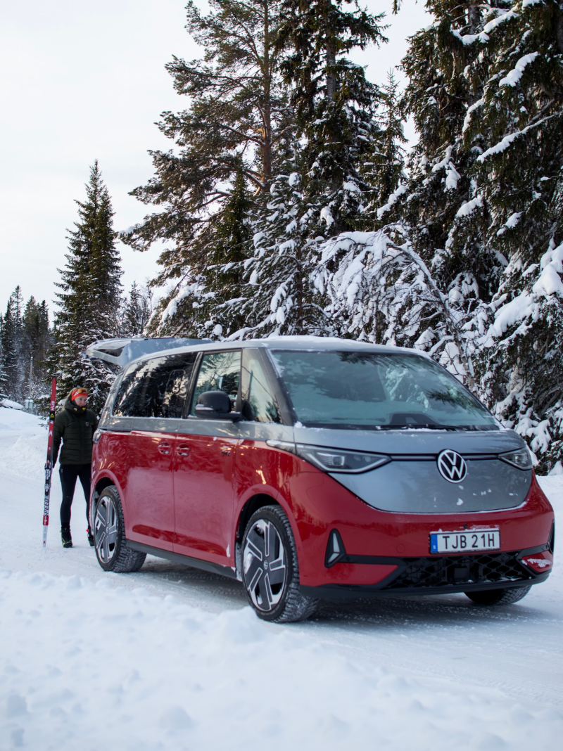 En kvinna står bakom en VW ID. Buzz GTX och ska packa in sina skidor