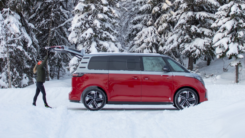 En kvinna öppnar bagageluckan på en VW ID. Buzz GTX i vinterlandskap