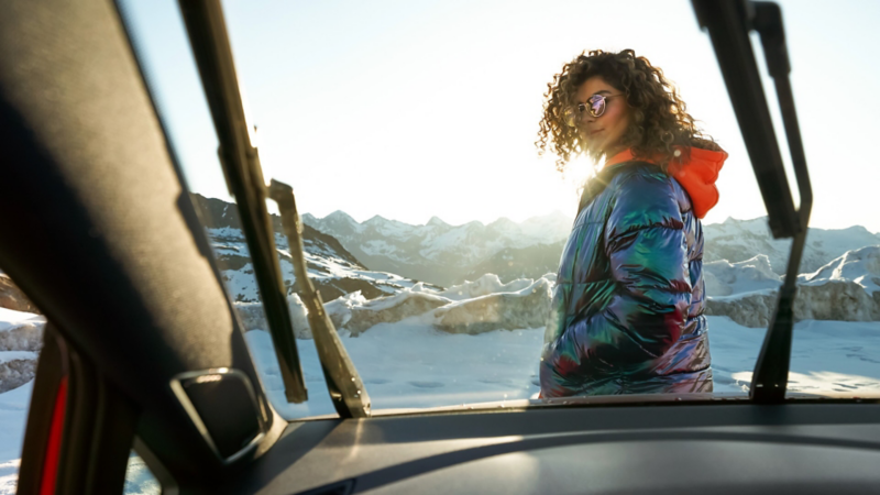 En kvinna med solglasögon står framför en VW med solsken i bakgrunden