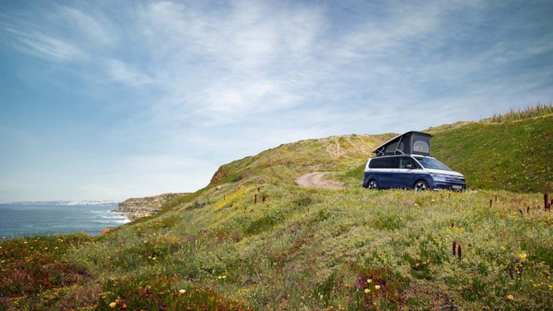 Nya VW California husbil med uppfällt popup-tak ute i naturen.