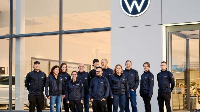 Personal från Team transportbilar uppställda framför ett VW showroom