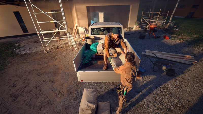 En arbetare står på flaket på en VW Transporter Pickup Dubbelhytt medan dennes kollega lämnar över en säck med bruk