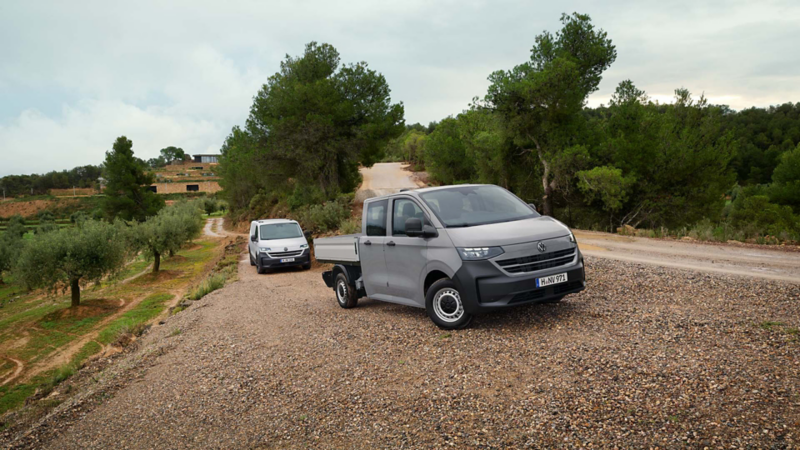 En VW Transporter Pickup dubbelhytt står framför en Transporter Skåp på en grusväg