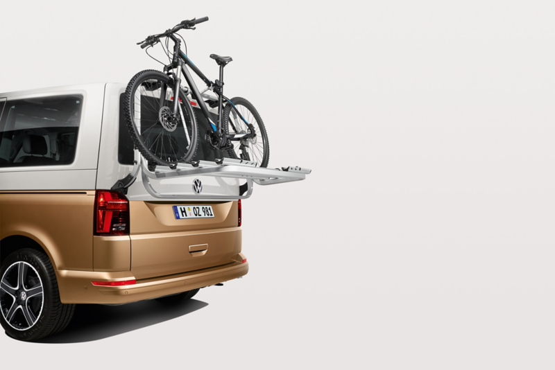  Un van Volkswagen bicolore (blanc et doré) est équipé d'un porte-vélos arrière transportant un VTT.