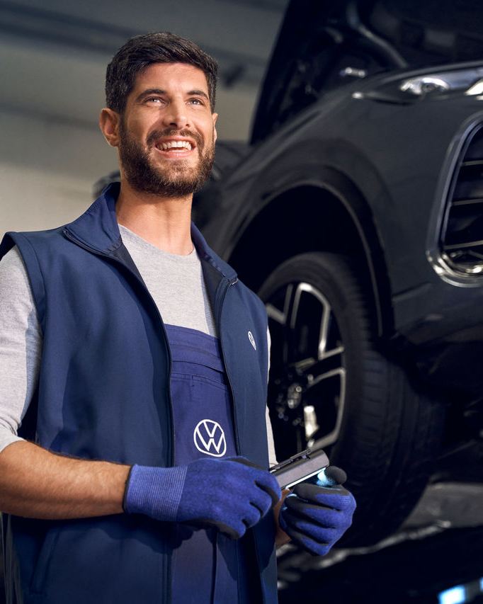 Ένας νέος άντρας μπροστά από ένα VW Tiguan, ελέγχει τους λαμπτήρες του κατά τη διάρκεια ενός Value Pack Service