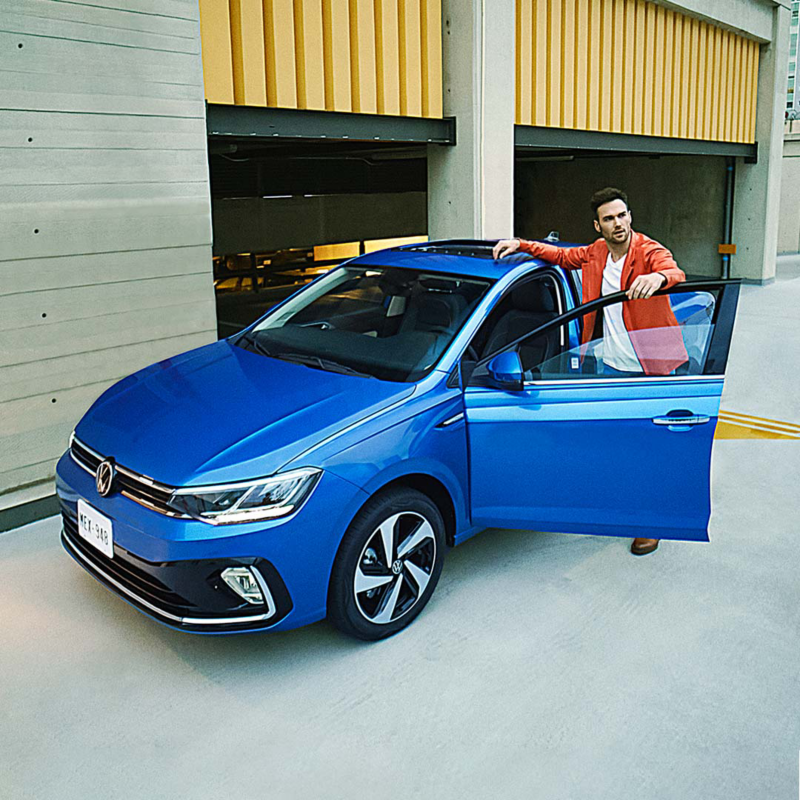 Virtus 2025 en color azul, con joven conductor a punto de abordar el auto sedán de Volkswagen. 