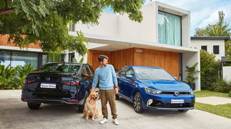 Imagen de dos autos sedán VW Virtus en colores azul frente a una casa junto con un hombre joven y un perro golden retriever