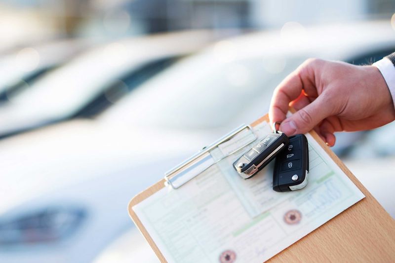 Autohändler hält Zulassungspapiere und Schlüssel vor einer Reihe von Fahrzeugen.