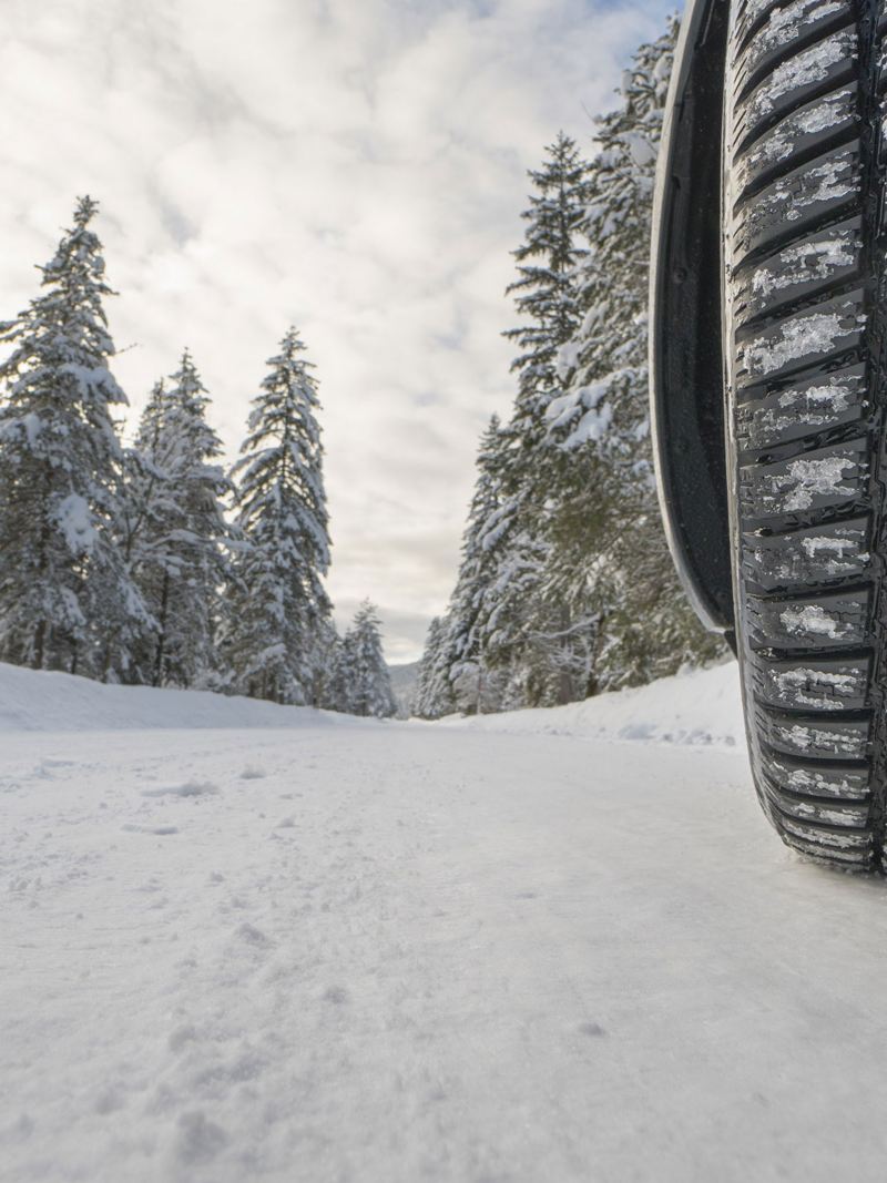Reifen eines Autos auf einer zugeschneiten Straße in einem Waldstück