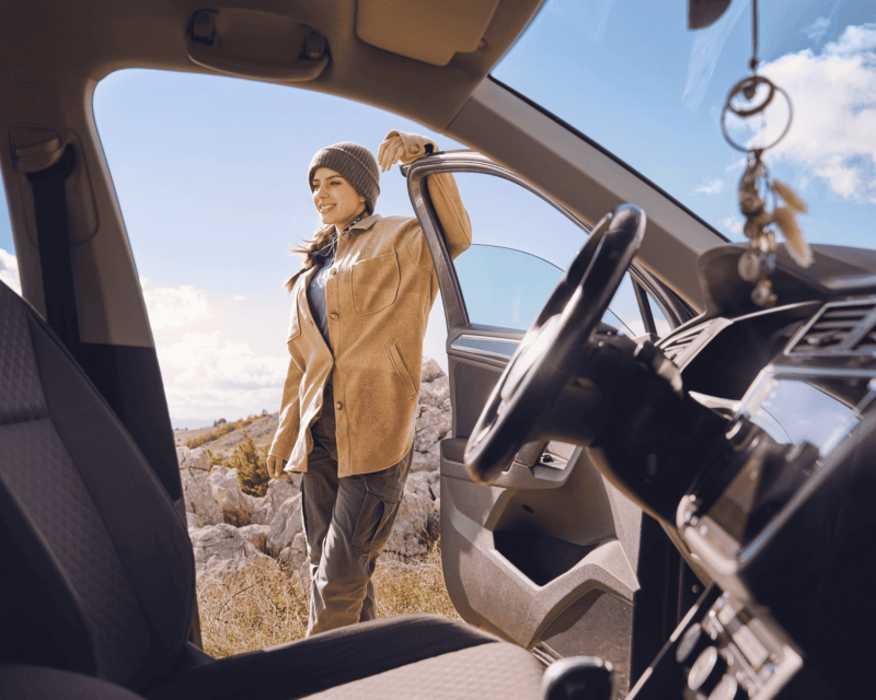 A woman stands by a Volkswagen vehicle, enjoying an outdoor adventure with beautiful scenery.