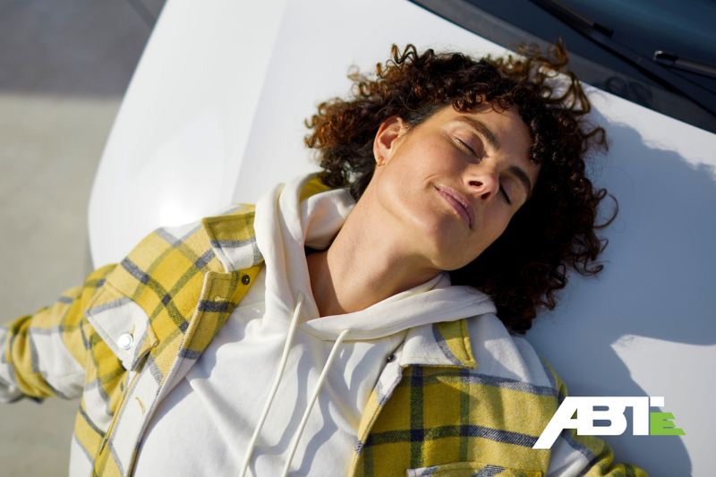 Eine Frau genießt die Sonne auf der Motorhaube des ABT e-Transpoorter 6.1.