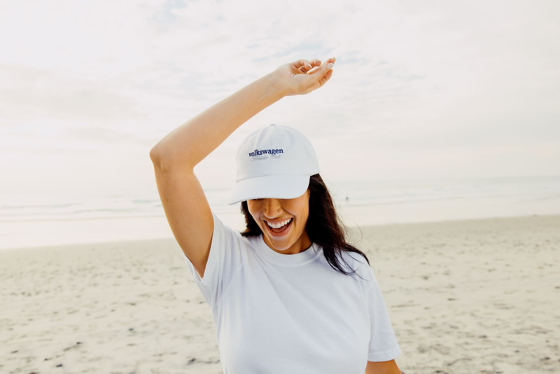 Persona con camisa blanca y gorra levanta el brazo en la playa, disfrutando del día.