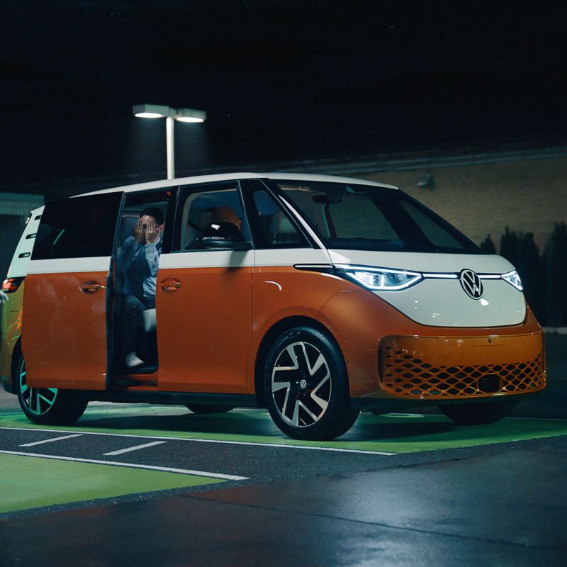 A Robot walks by an orange European Model ID.Buzz parked at an Elctrify Canada Charger. 