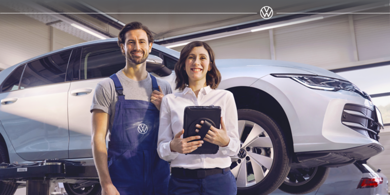 A dealer and a mechanic smile at the camera in a shop 