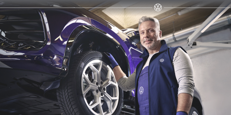 Un mécanicien souriant en train de travailler sur une voiture bleue.