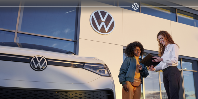 A dealer showing a woman information next to a white car 