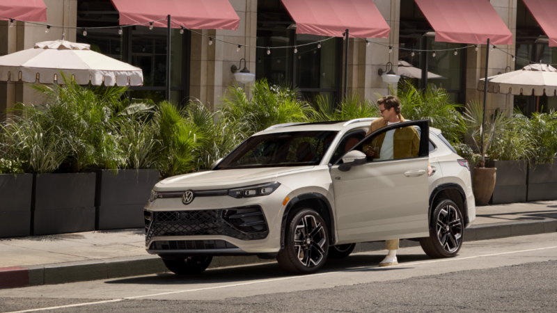 A man sliding into the front seat of a white parked car.