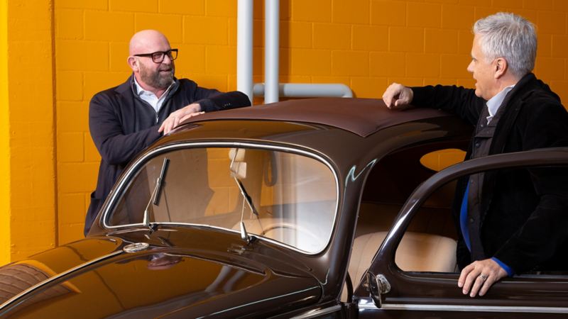Dino Graf und Claude Gregorini diskutieren aufgestützt auf einem VW Käfer.