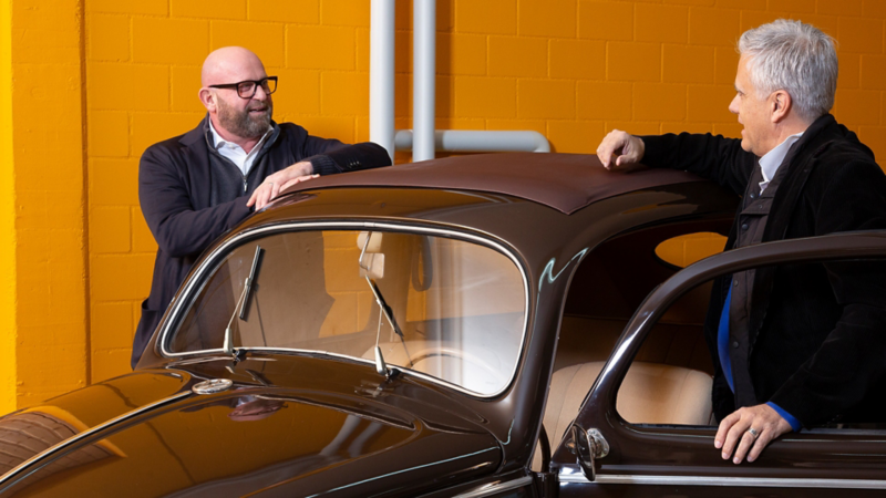 Dino Graf und Claude Gregorini diskutieren aufgestützt auf einem VW Käfer.