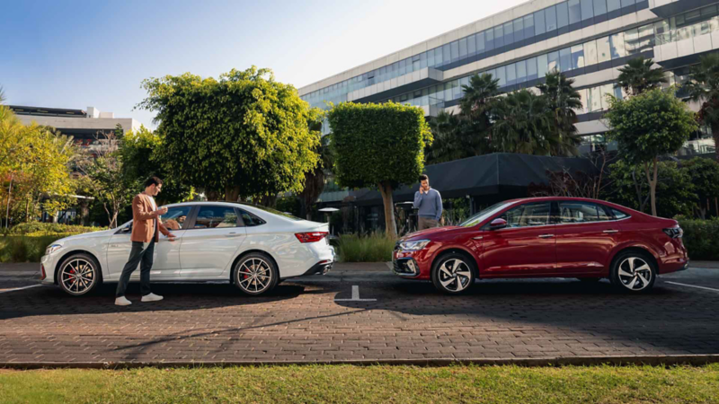 Dos hombres posan a lado de vehículos sedanes de Volkswagen.