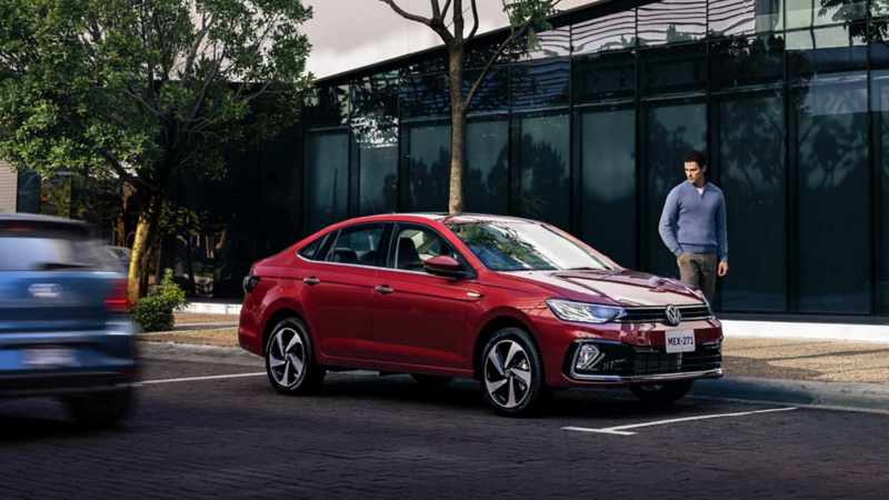 Hombre camina a lado de Virtus Volkswagen color rojo.