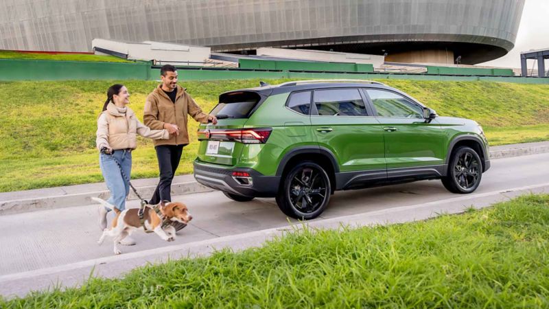 Pareja con un perro caminan alrededor de Nuevo Taos 2025, SUV en color verde.