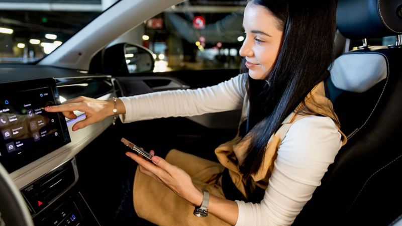 Nuevo Taos 2025. Mujer sentada en el asiento de copiloto toca la pantalla touch semiflotante de camioneta SUV. 