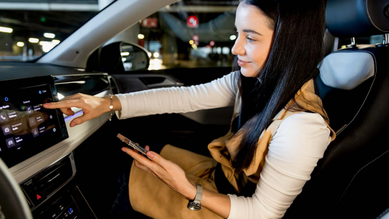 Nuevo Taos 2026. Mujer sentada en el asiento de copiloto toca la pantalla touch semiflotante de camioneta SUV. 