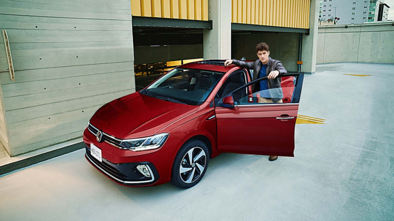 Virtus 2026 en color rojo, con joven conductor a punto de abordar el auto sedán de Volkswagen. Modificado con inteligencia artificial