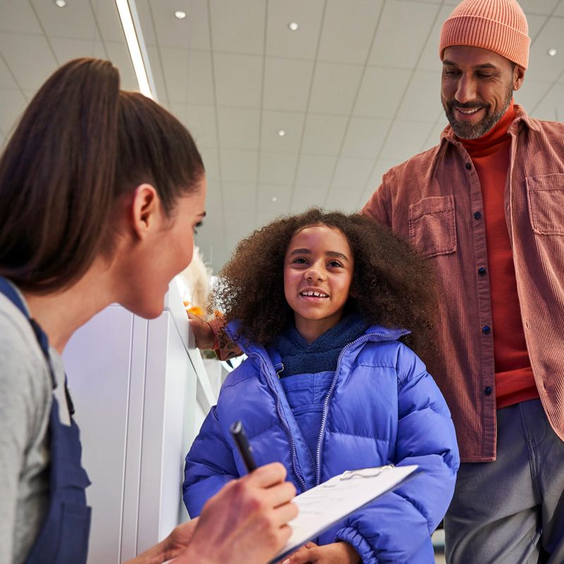 Un père et sa fille parlent à une représentante du service à la clientèle VW