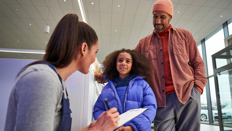 Un père et sa fille parlent à une représentante du service à la clientèle VW