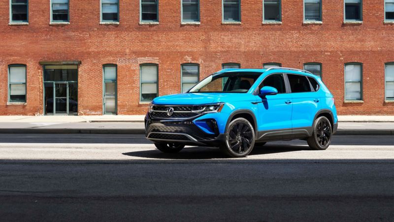 A blue 2024 VW Taos parked in front of a brick building