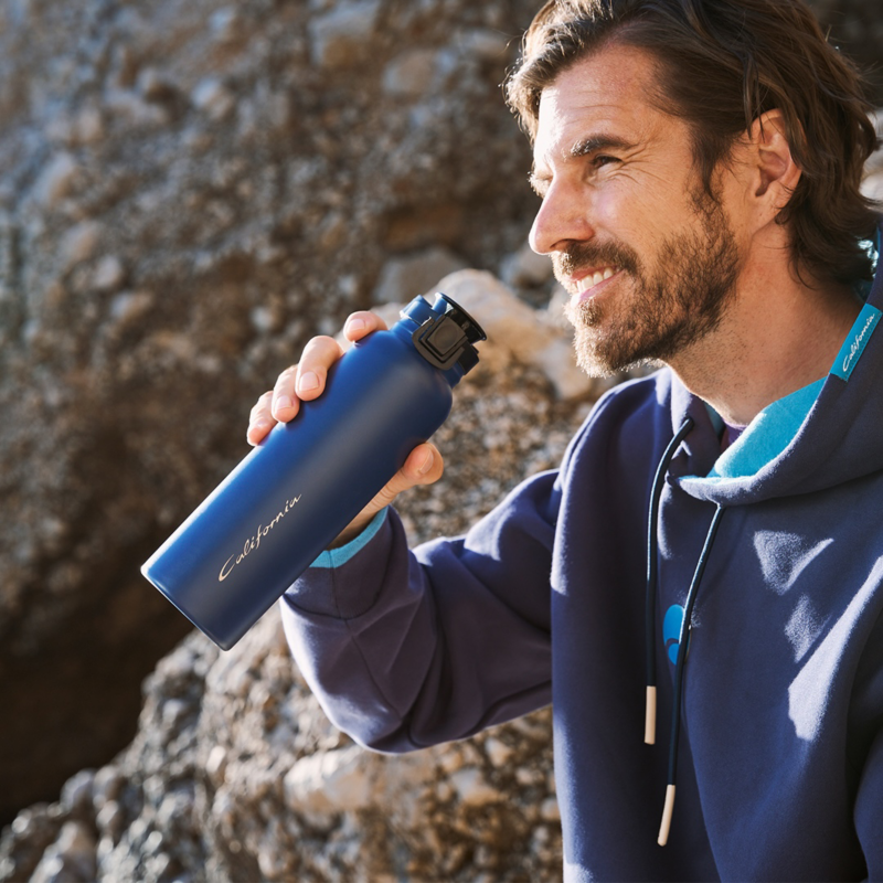 A man sitting on a rocky area and drinking from a water bottle. 