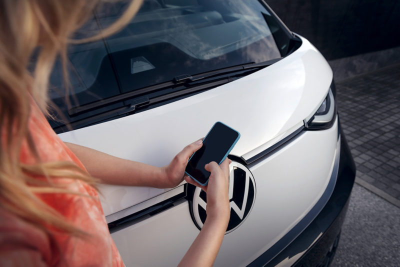 Kobieta trzyma smartfon w rękach na tle maski Volkswagena ID. Buzz.