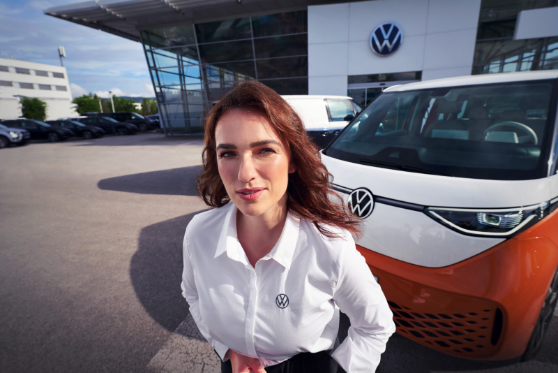 Pracownica salonu przed budynkiem na tle Volkswagena ID. Buzz.