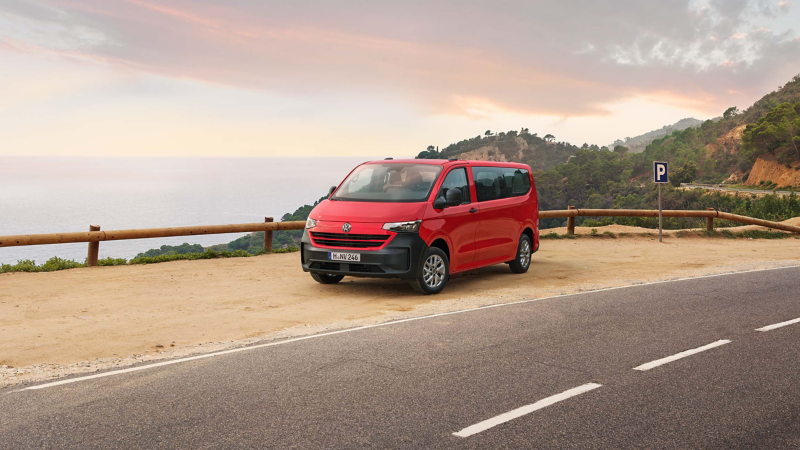 En röd VW Caravelle minibuss står parkerad vid havet