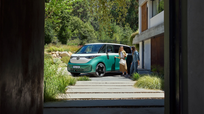 Två kvinnor står bredvid en grönvit VW ID Buzz med lång hjulbas