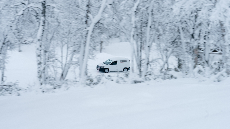 En vit VW Caddy Cargo med logo Berggren Bygg kör på vinterväg